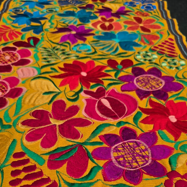 Colorful floral patterned table runner with vibrant colors on a yellow background. Oaxaca Mexico.
