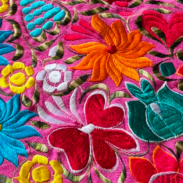 Close up of Oaxaca table runner showing floral embroidery pattern with a pink background