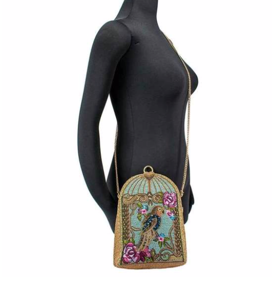 Mannequin carrying a blue beaded handbag featuring a detailed parrot design with floral patterns and a gold-tone cage-like structure by Mary Frances.