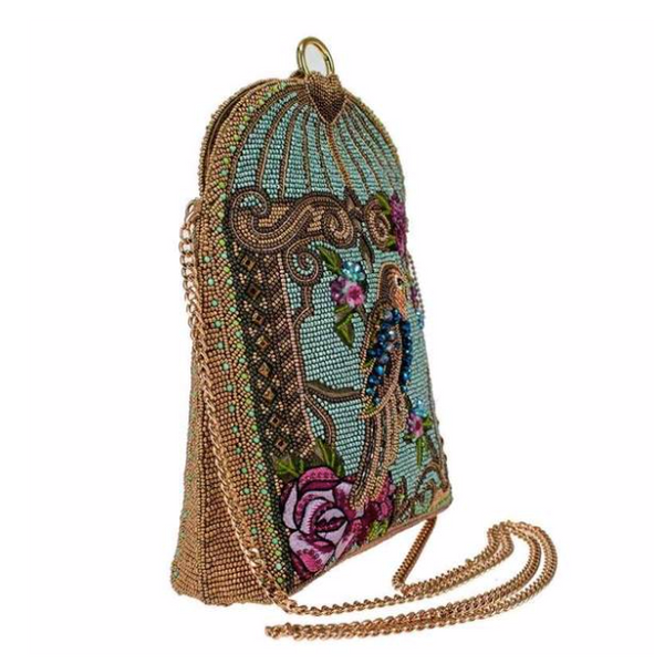 Left angle of a blue beaded handbag featuring a detailed parrot design with floral patterns and a gold-tone cage-like structure and chain starp by Mary Frances.