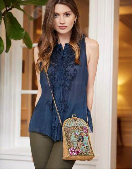 A Model showing a blue beaded handbag featuring a detailed parrot design with floral patterns and a gold-tone cage-like structure by Mary Frances.